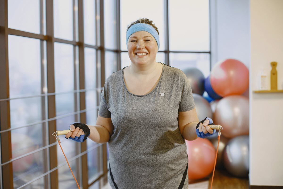 Smiling woman exercising with jump rope in a gym, with stability balls in the background
