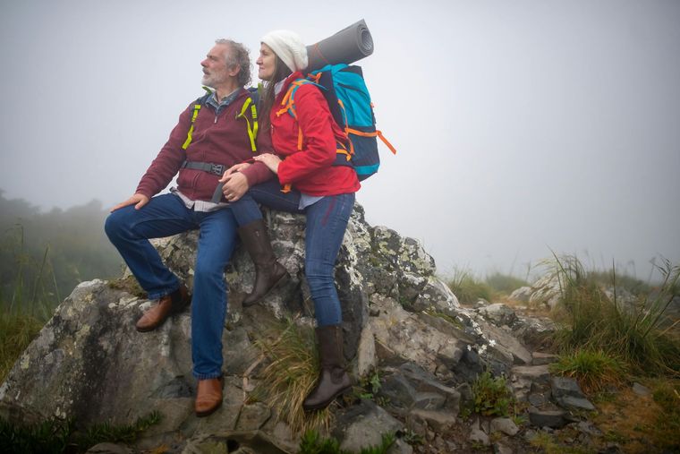 Couple hiking, sitting on a rock. One wears a backpack and looks at the foggy vista.