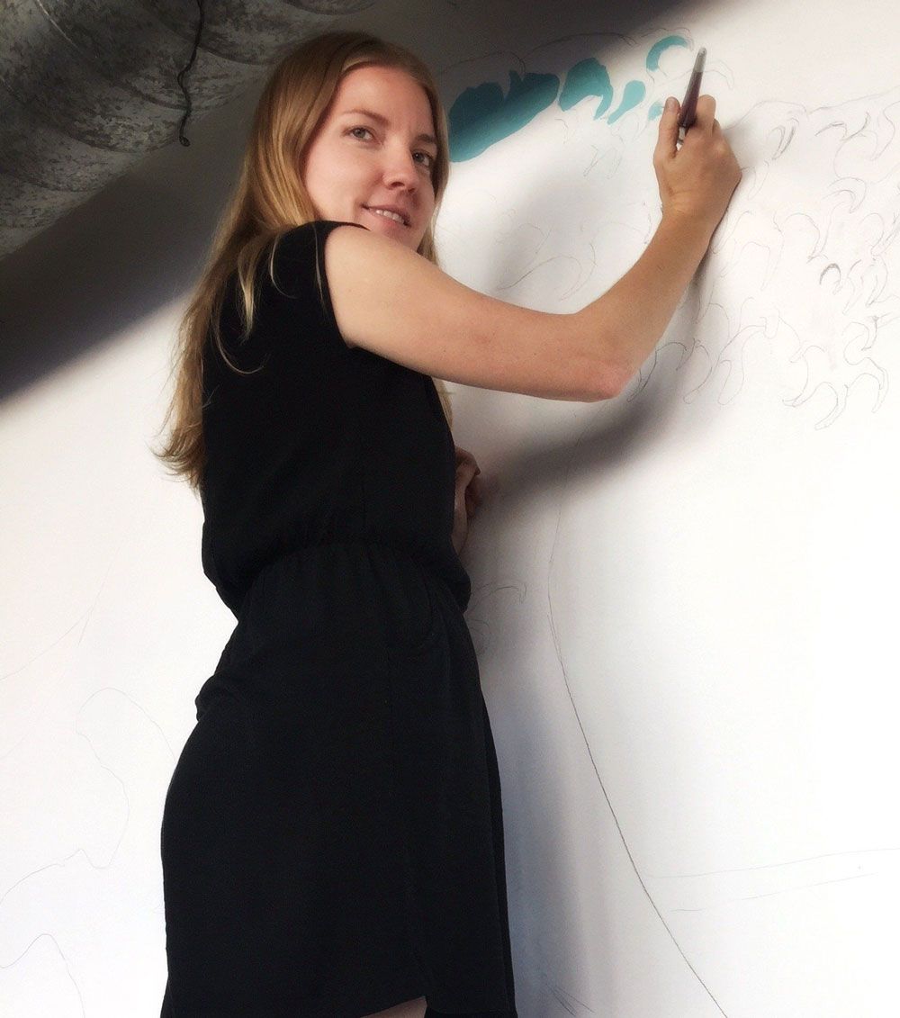 Woman in black dress painting on a white wall.