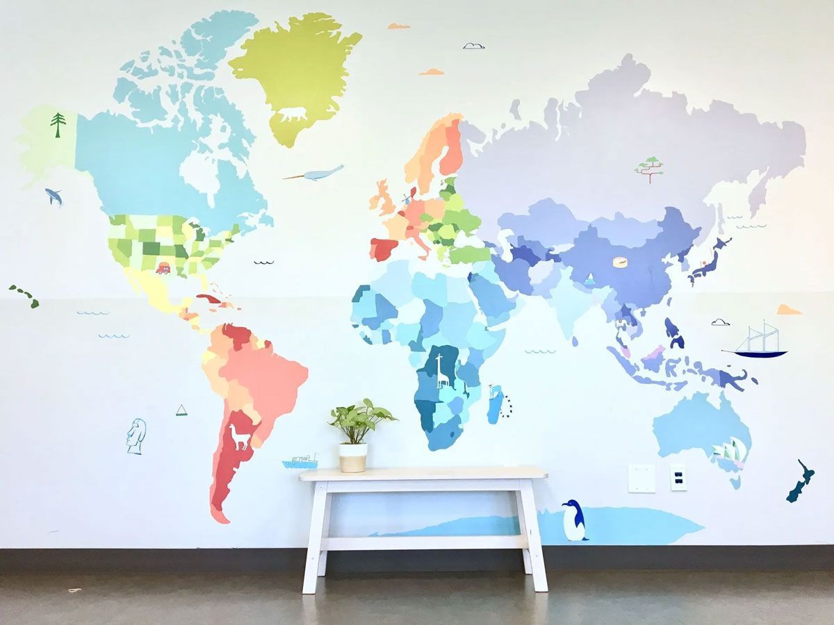 Colorful world map decal on a white wall with a small table and a plant.