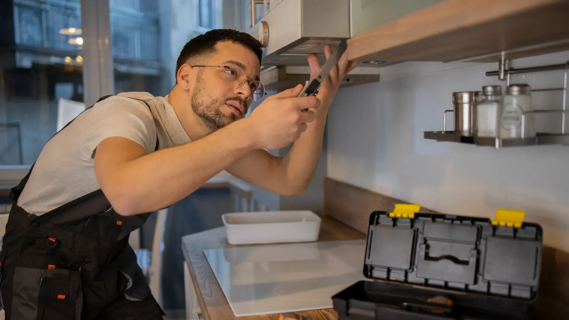 A man is fixing a kitchen hood with a screwdriver.