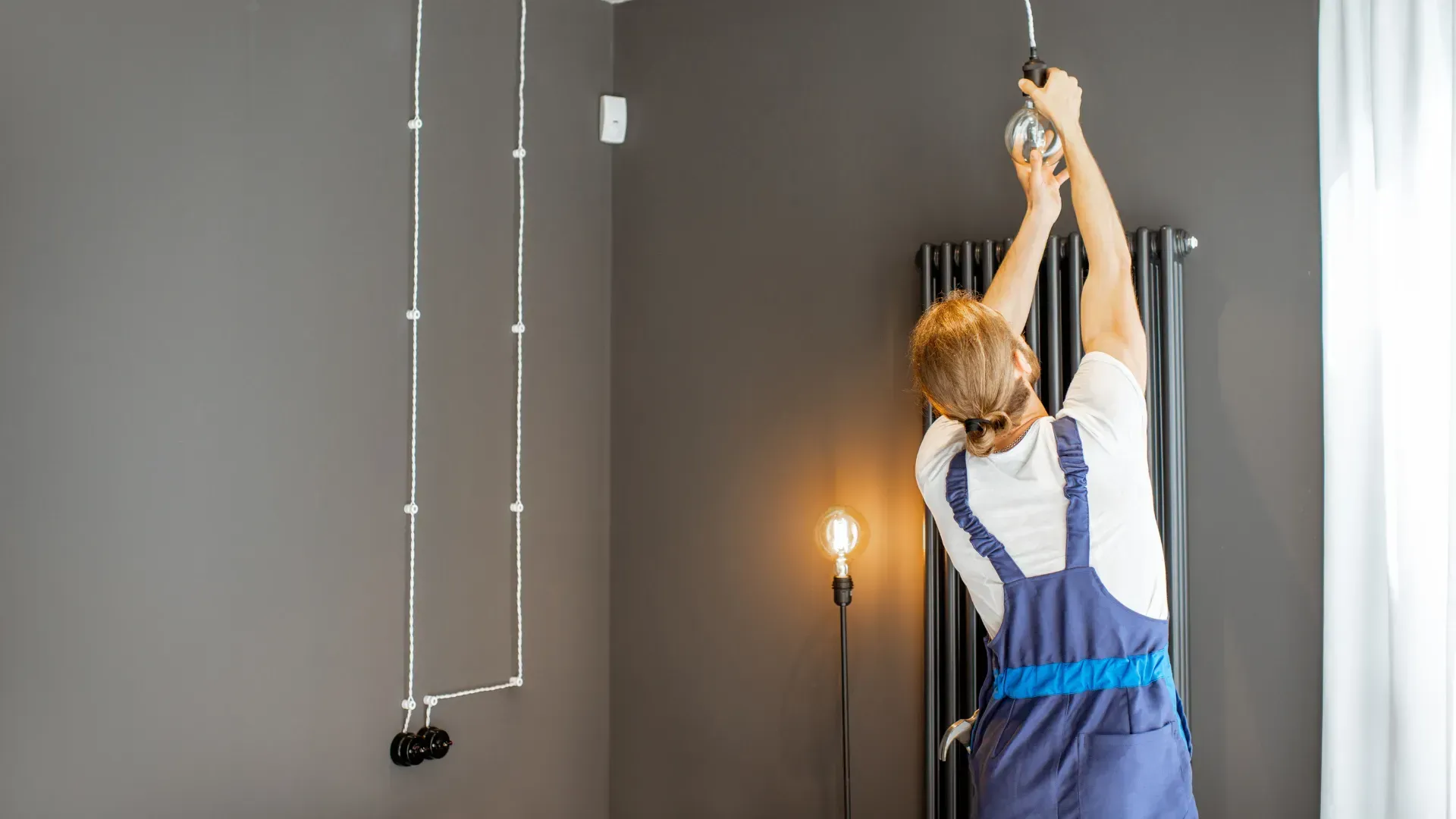A man is hanging a light bulb from the ceiling in a room.