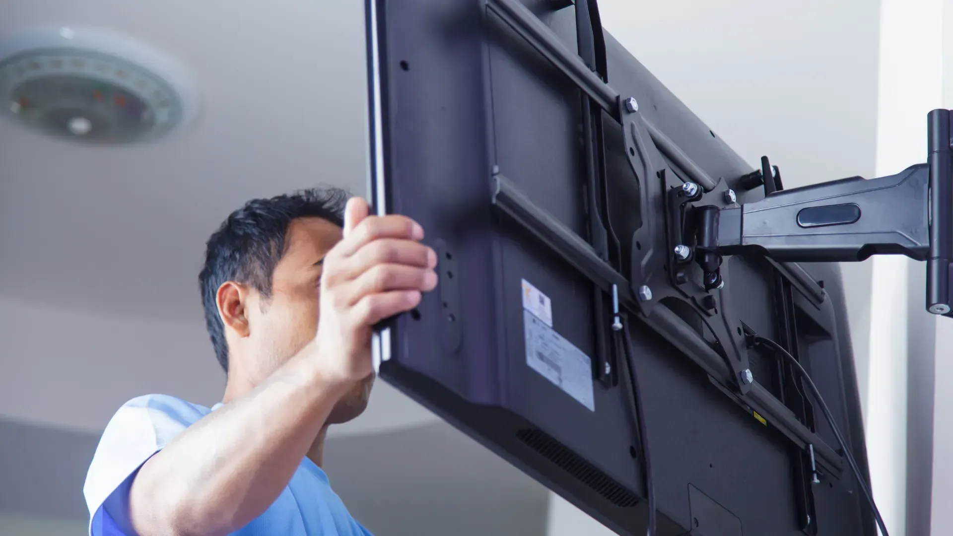 A man is installing a flat screen tv on a wall.