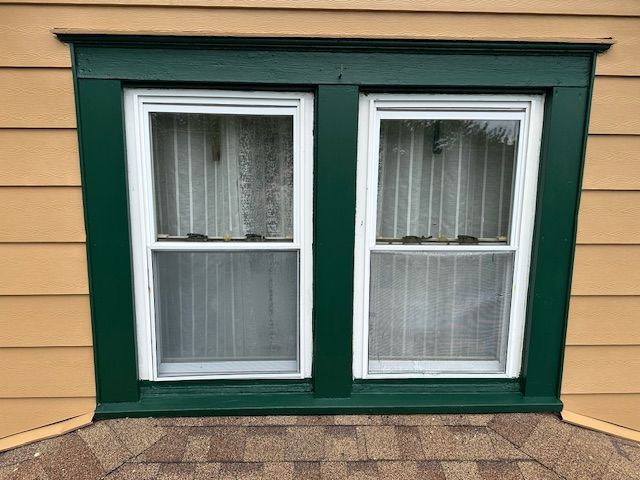 A window with a green frame is on the side of a house.