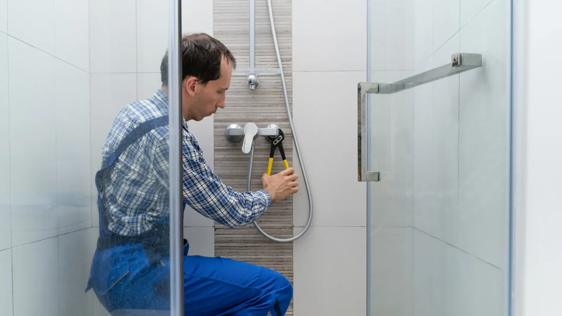 A man is fixing a shower head in a bathroom.