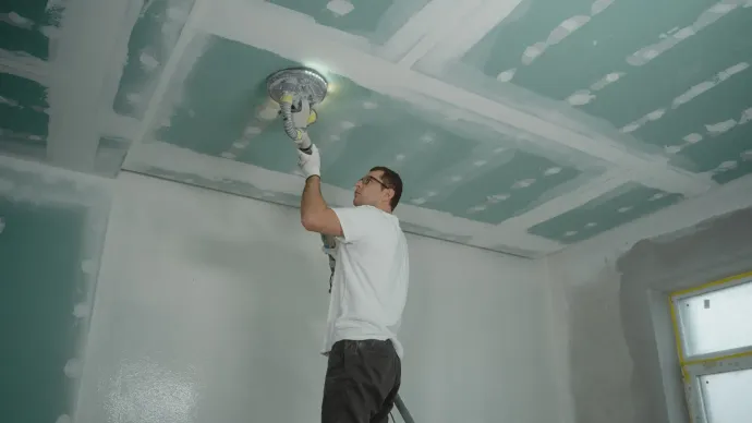A man is standing on a ladder painting a ceiling.