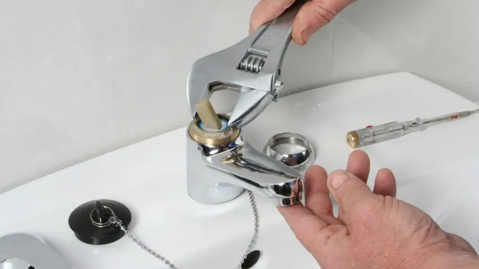 A person is fixing a sink faucet with a wrench.