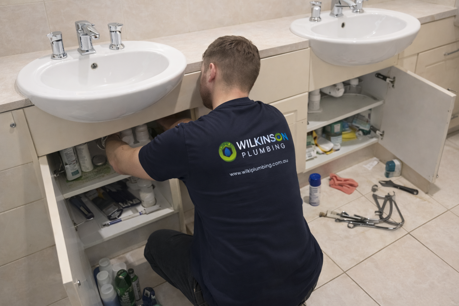 Plumber working under a bathroom sink, installing or repairing plumbing.