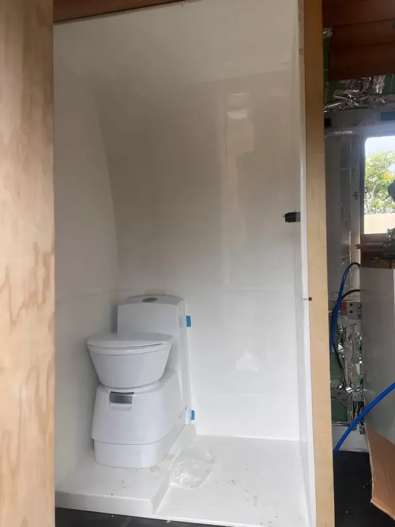 White composting toilet inside a small, white-walled bathroom.