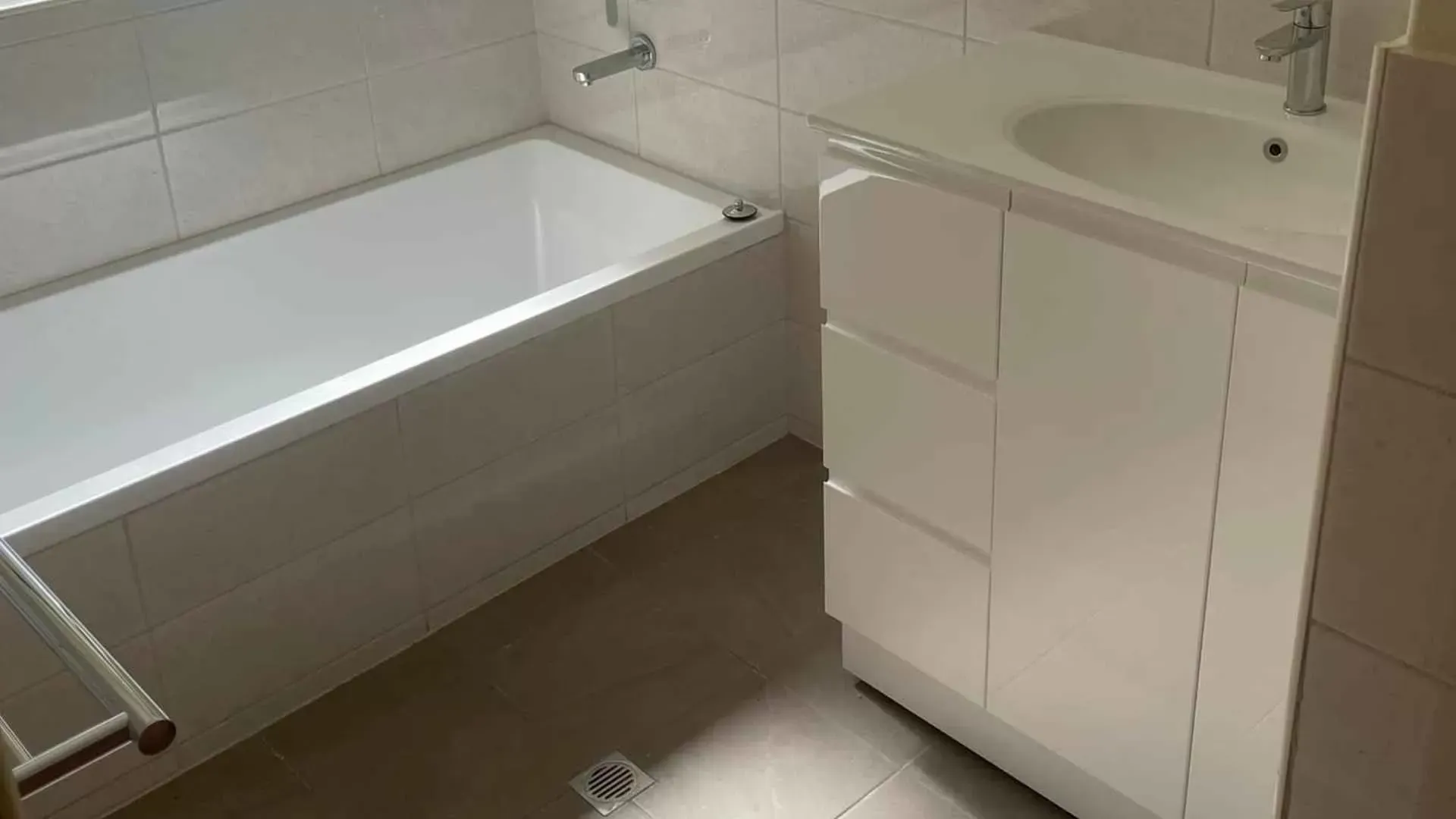 White bathroom with a tub, vanity with sink, and light-colored tiled floor.