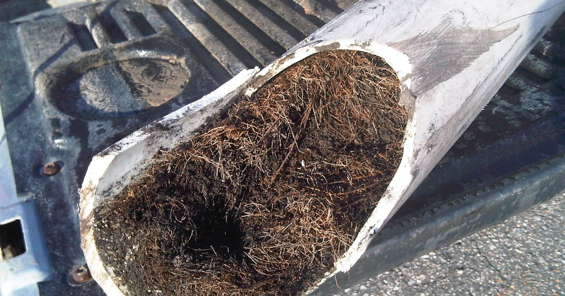 Cut-open white pipe filled with a dense, brown, fibrous mass. Resting on a dark surface.
