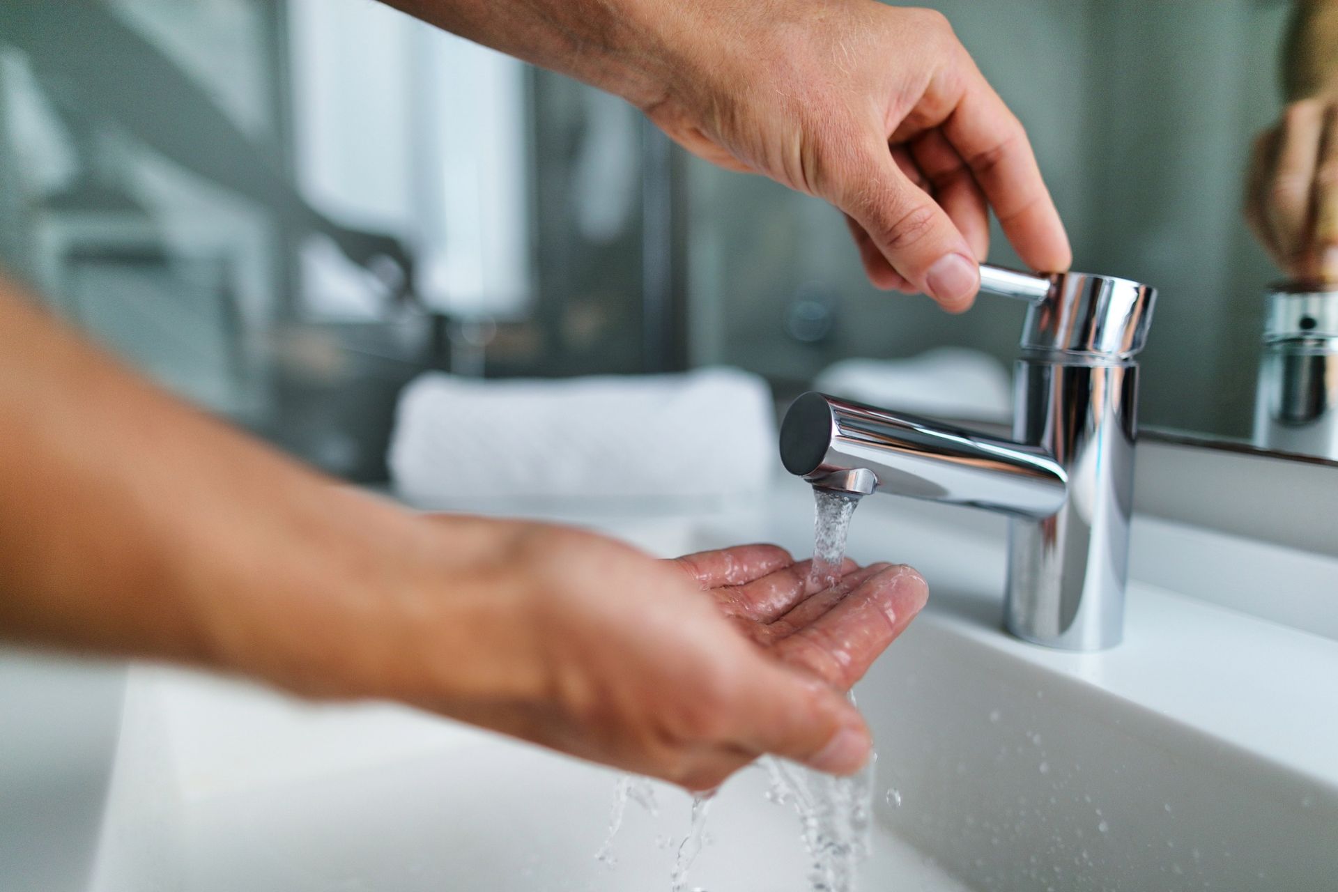 Person washing hands in a bright bathroom with a silver faucet. Water streams into their open palm.