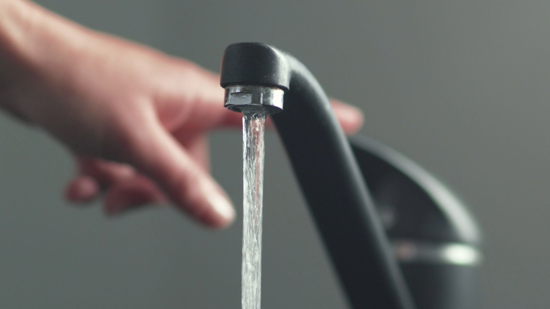 Water flowing from a black faucet; a hand reaches toward it.