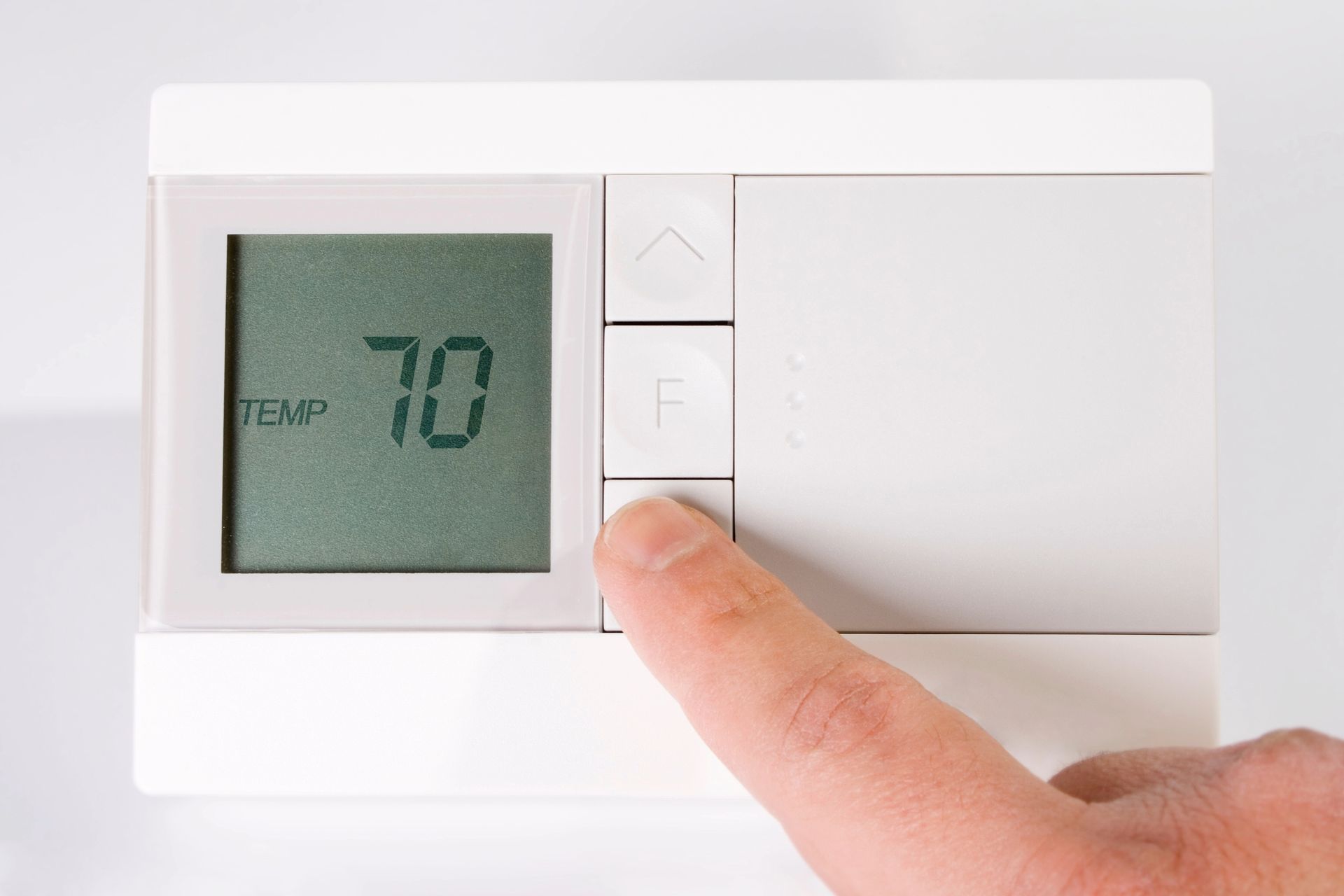 A person's finger presses the Fahrenheit button on a digital thermostat, which reads 70 degrees.
