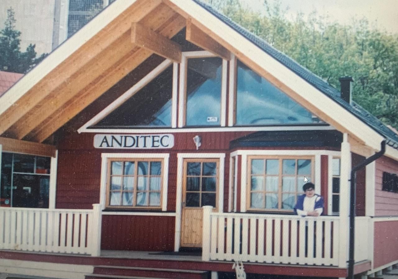 Edificio de madera rojo y blanco con techo puntiagudo y gran ventanal triangular; un niño está de pie en el porche.