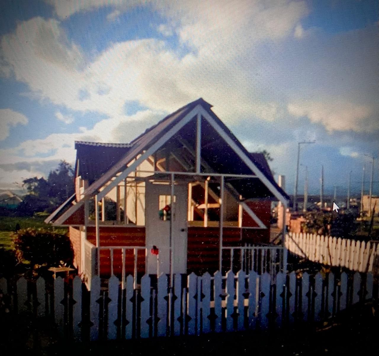 Una casa de juegos roja y blanca con una valla de estacas bajo un cielo nublado.