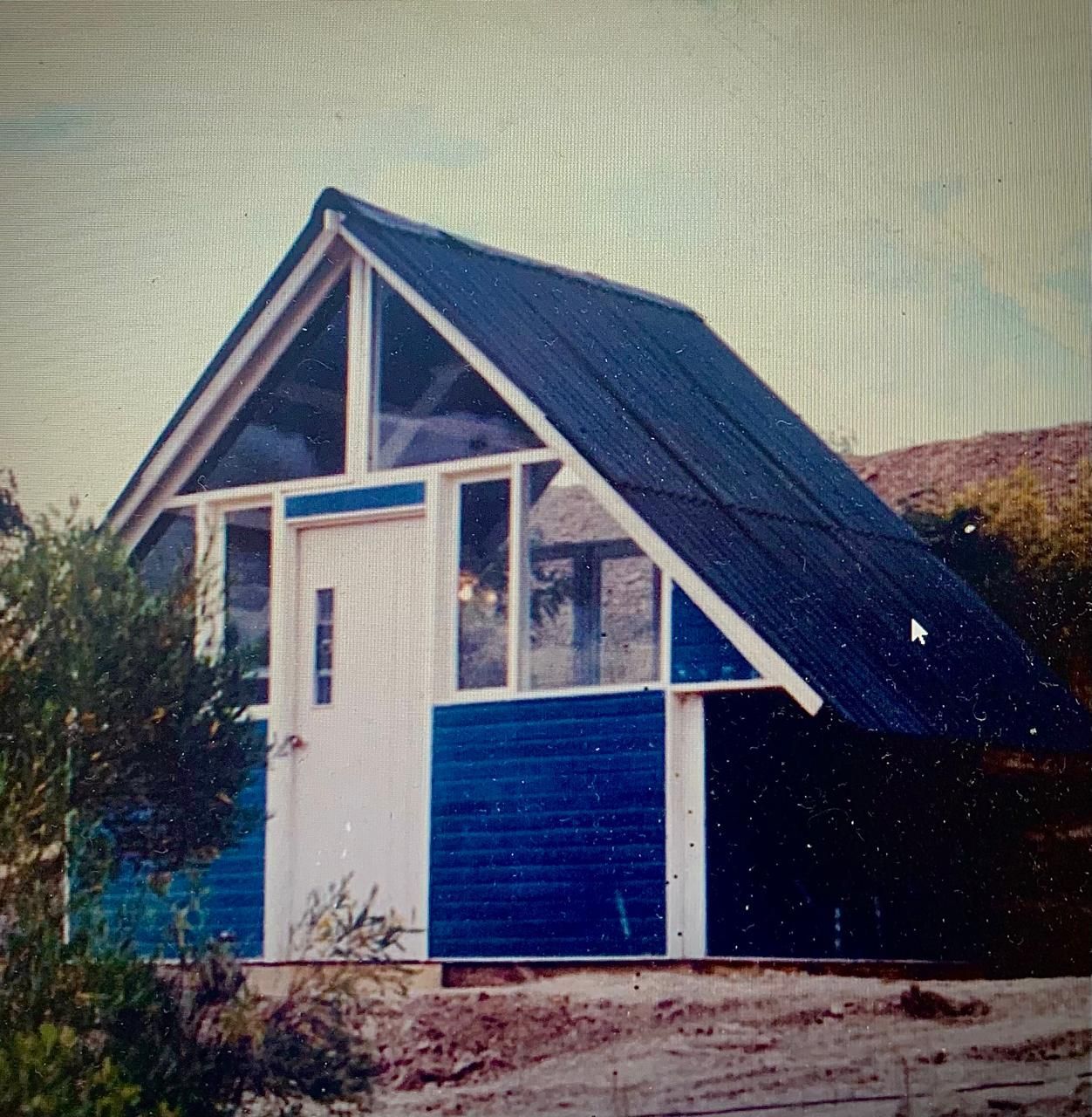 Cabaña azul y blanca en forma de A con techo en ángulo y ventana triangular.
