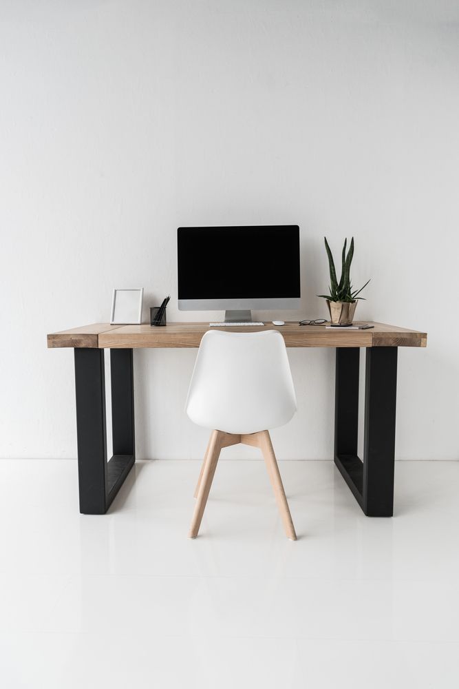 Espacio de trabajo moderno con escritorio de madera, monitor negro, silla blanca y planta en maceta.