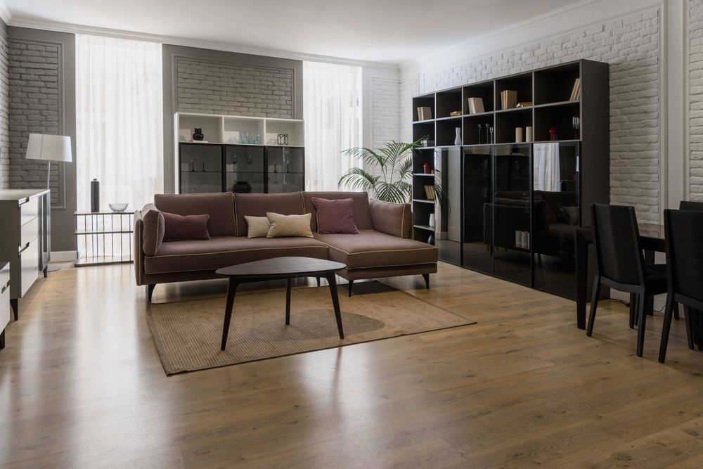 Sala de estar con sofá marrón, estantes negros y piso de madera.