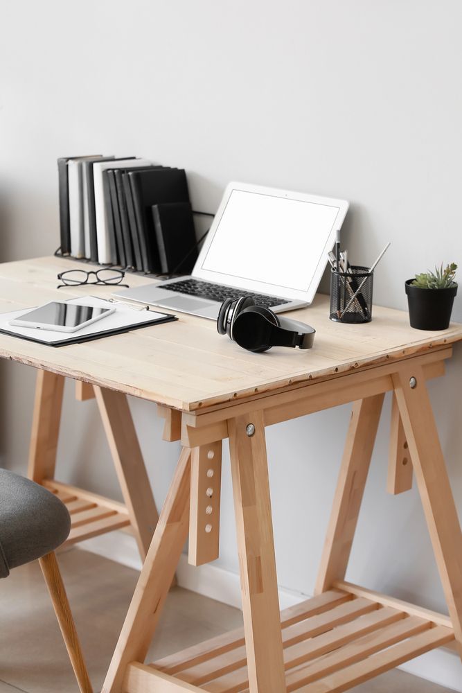 Escritorio de madera con portátil, auriculares, libros y tableta. Fondo de pared blanco.