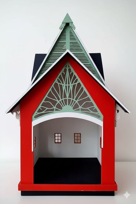 Edificio en miniatura de color rojo y blanco con entrada abierta, techo verde y negro y ventanas pequeñas.