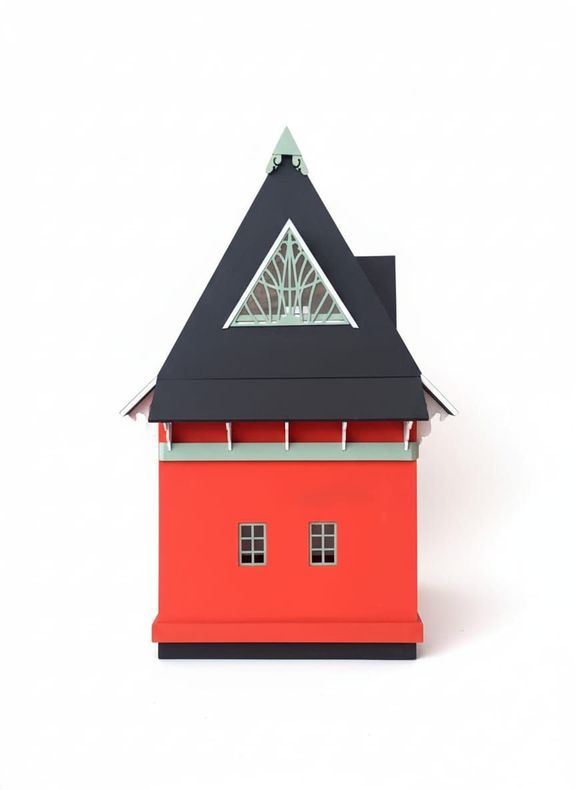 Maqueta de edificio de color rojo y negro con techo triangular y pequeñas ventanas.