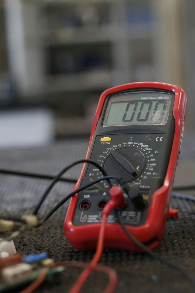 Red digital multimeter with probes on a workbench, displaying 000.