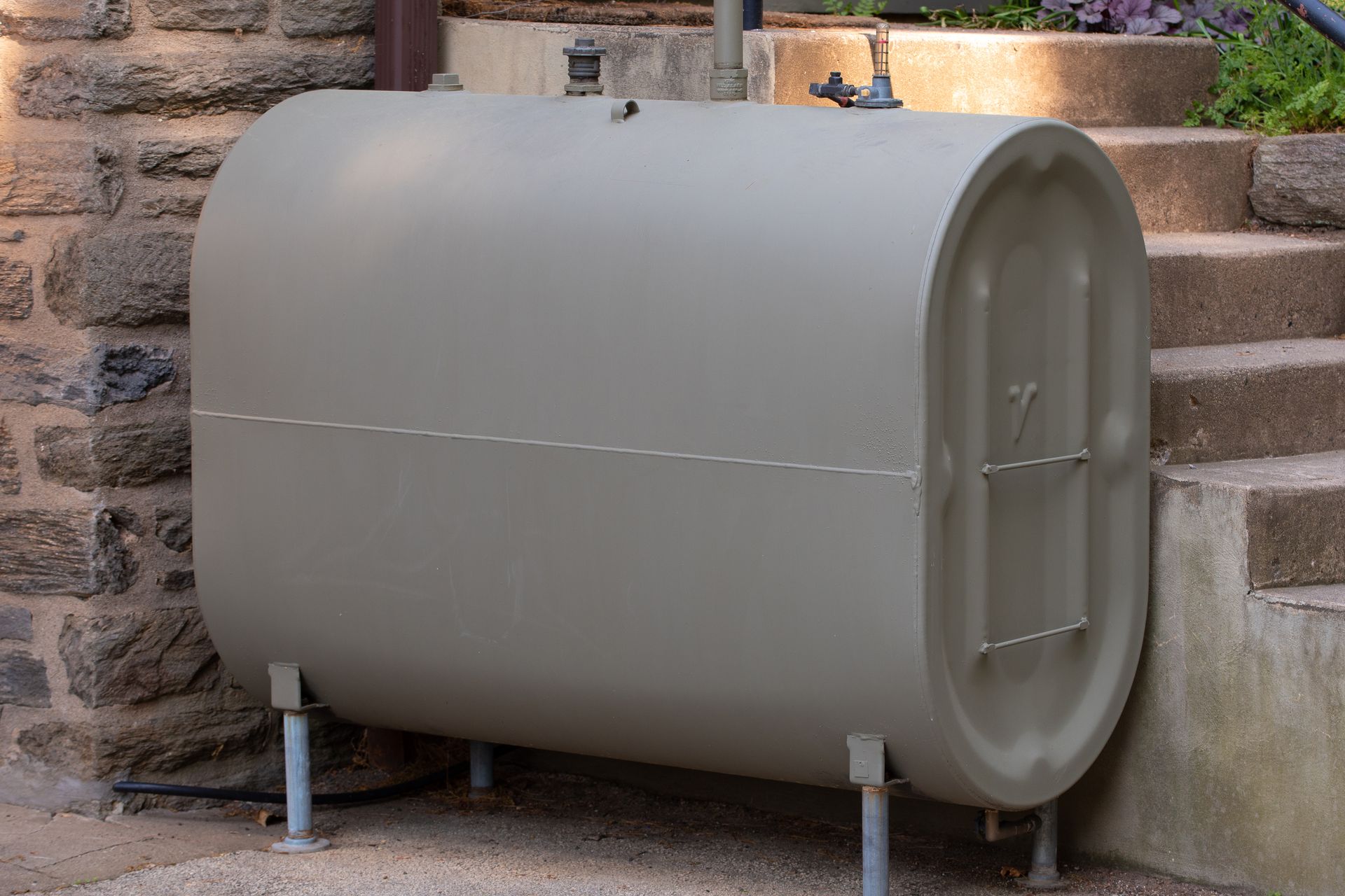 Outdoor oil storage tank installed beside stone wall near concrete steps.