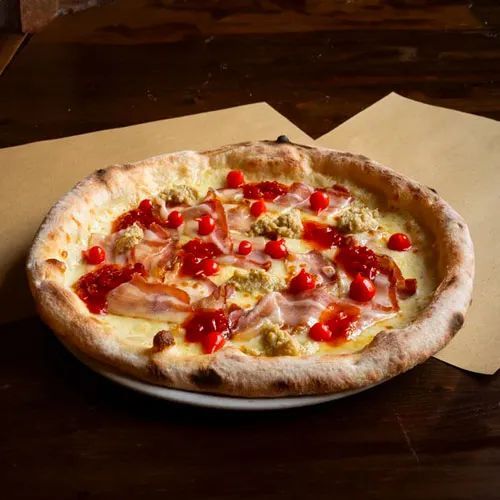 Una pizza con pomodori, pancetta e formaggio su un piatto su un tavolo.