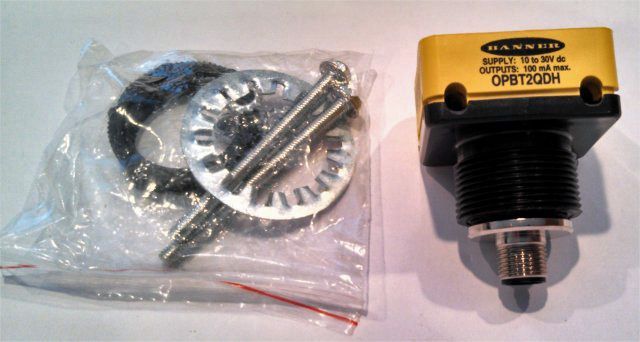 Plastic bag with small metal parts beside a yellow-and-black sensor device on a white surface
