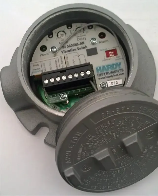 Open electric meter with gray cover and visible terminal block inside a wall recess