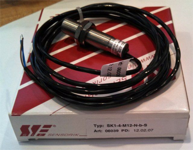 Black cylindrical sensor with cable coiled on a white-and-red box