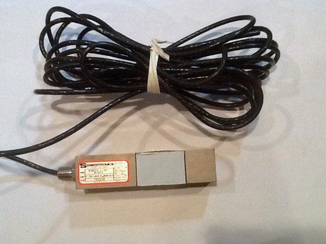 Coiled black cable with a small rectangular sensor or foot pedal on a beige surface