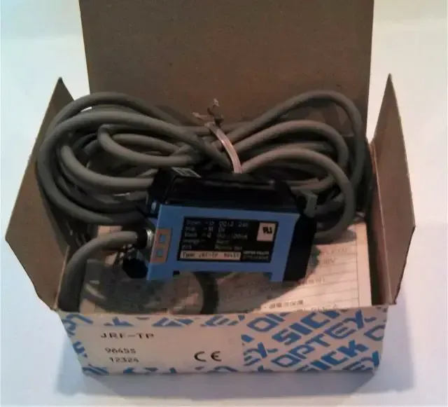 Black electronic device with coiled cables in a cardboard box, viewed from above