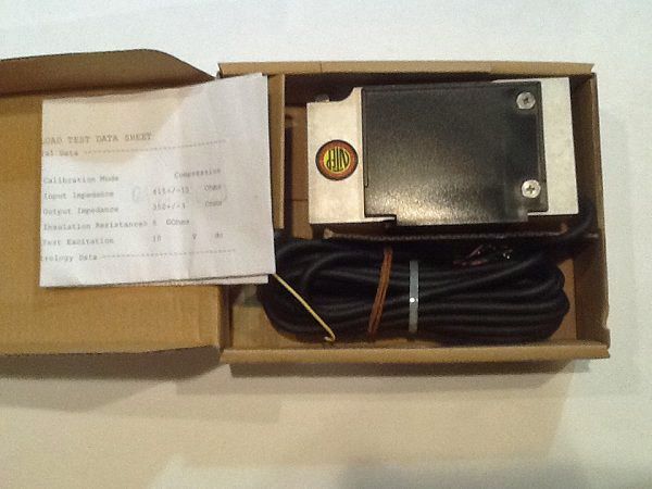 Open cardboard box with a small metal device, coiled cable, and folded instructions inside