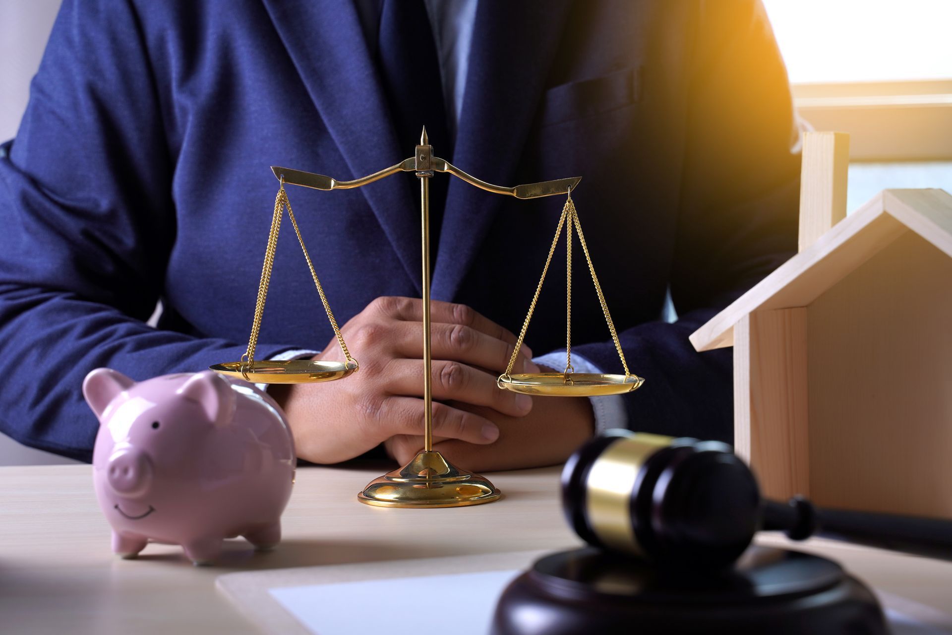 Scales of justice, gavel, house model, and piggy bank on desk, representing estate planning. Scales of justice, gavel, house model, and piggy bank on desk, representing estate planning.