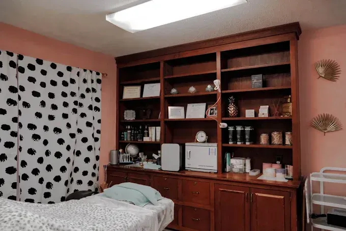 Aesthetician's room with treatment bed, large wooden shelf holding products and supplies, and polka dot curtains.
