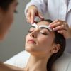 Woman getting her eyebrows shaped at a salon. A person is holding stencils over the eyebrows.