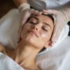 Woman receiving a facial treatment with a mask on, eyes closed, lying on a white towel.