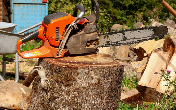 Orange chainsaw resting on a freshly cut wood stump.