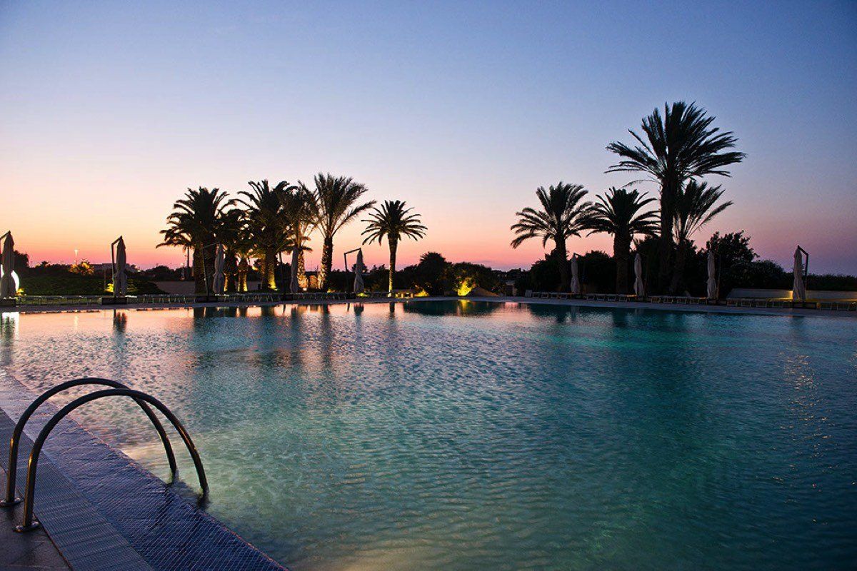 Una grande piscina circondata da palme al tramonto