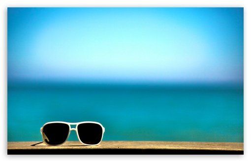 Un paio di occhiali da sole sopra un tavolo di legno con il mare sullo sfondo