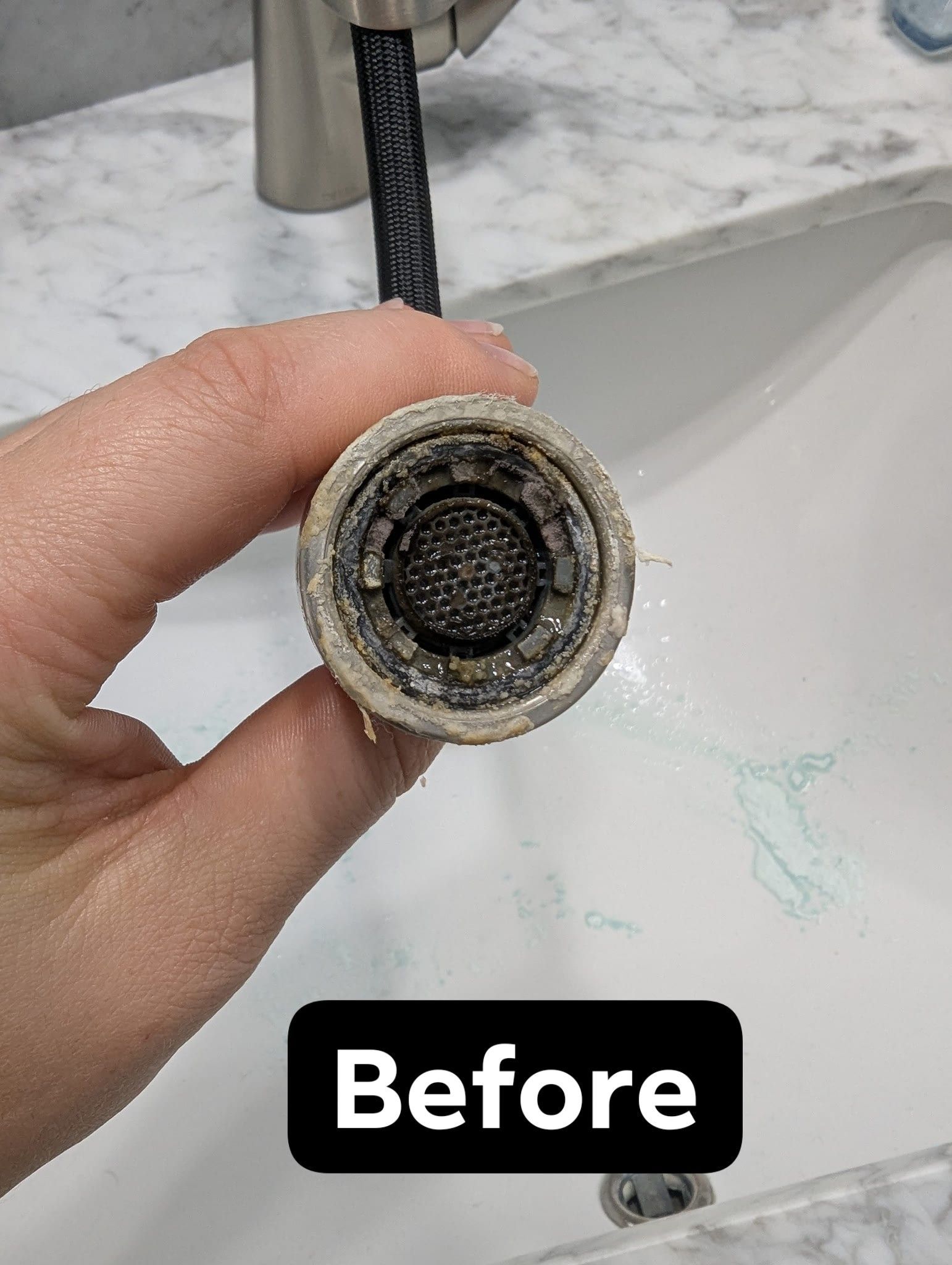 Hand holding a faucet aerator clogged with mineral buildup, above a bathroom sink.