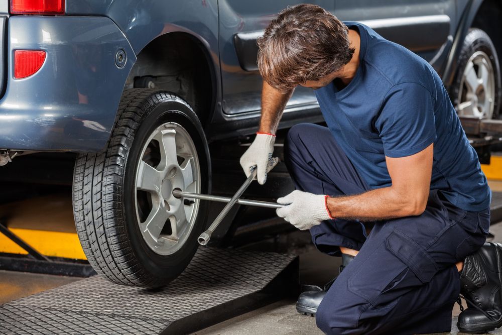 Mechanic Kneeling Beside a Car, Using a Lug Wrench to Change a Tyre — Edmonton Tyre and Mechanical Services in Edmonton, QLD