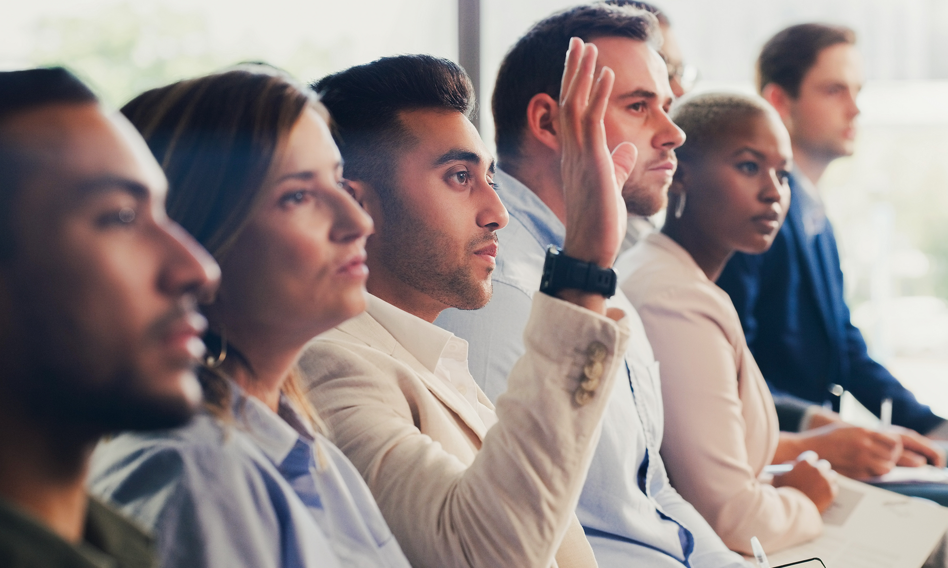 Attendees at a conference, one man raises hand.