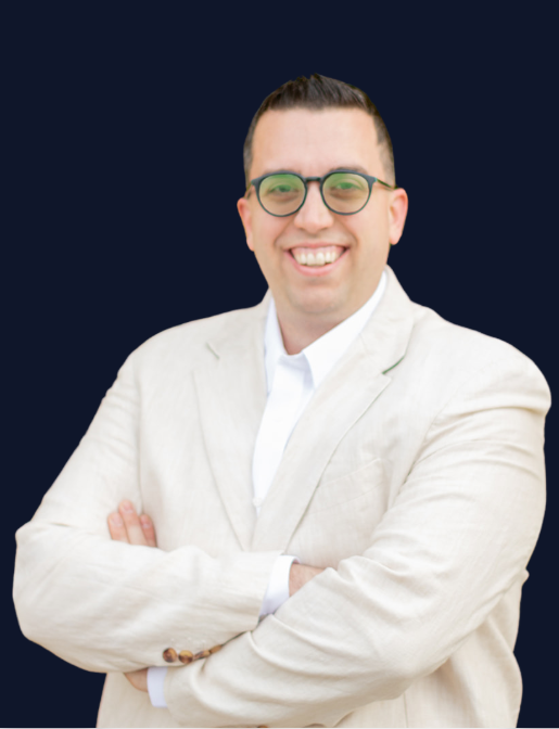 A man in a suit and glasses is smiling with his arms crossed