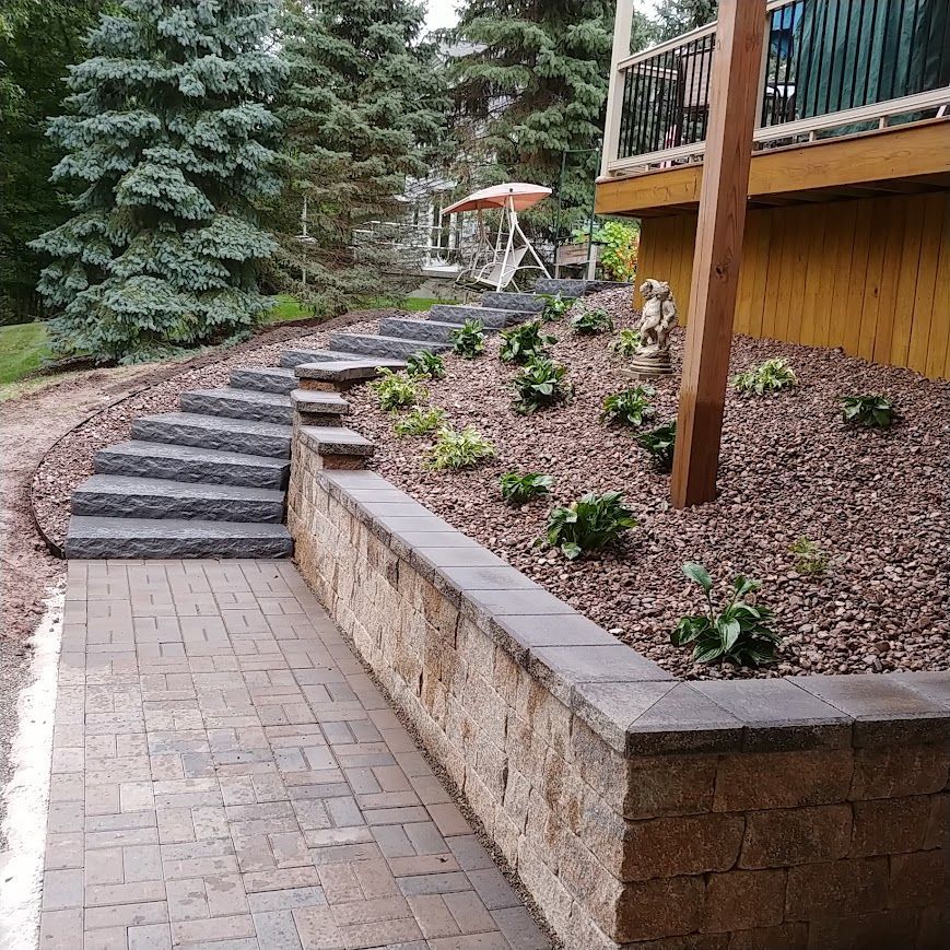 Stone steps and retaining wall leading to a deck, with landscaping and trees.