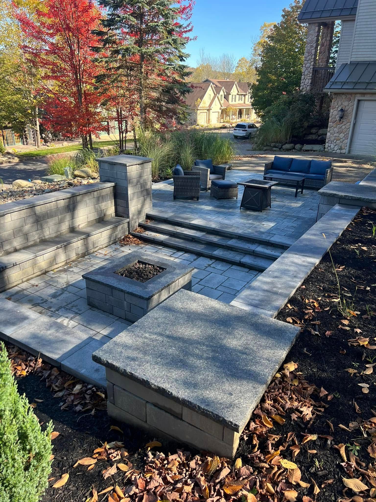 Outdoor patio with fire pit, seating, and steps, surrounded by landscaping and autumn trees.