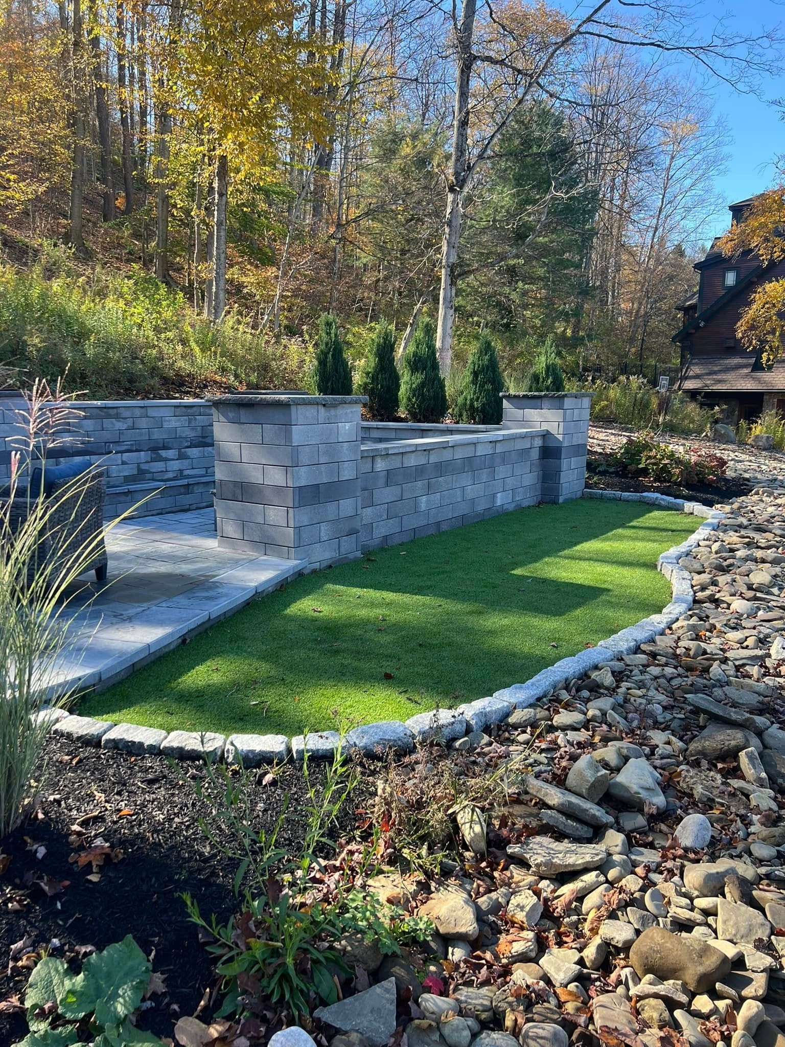 Stone retaining wall with a small lawn, and trees in the background.