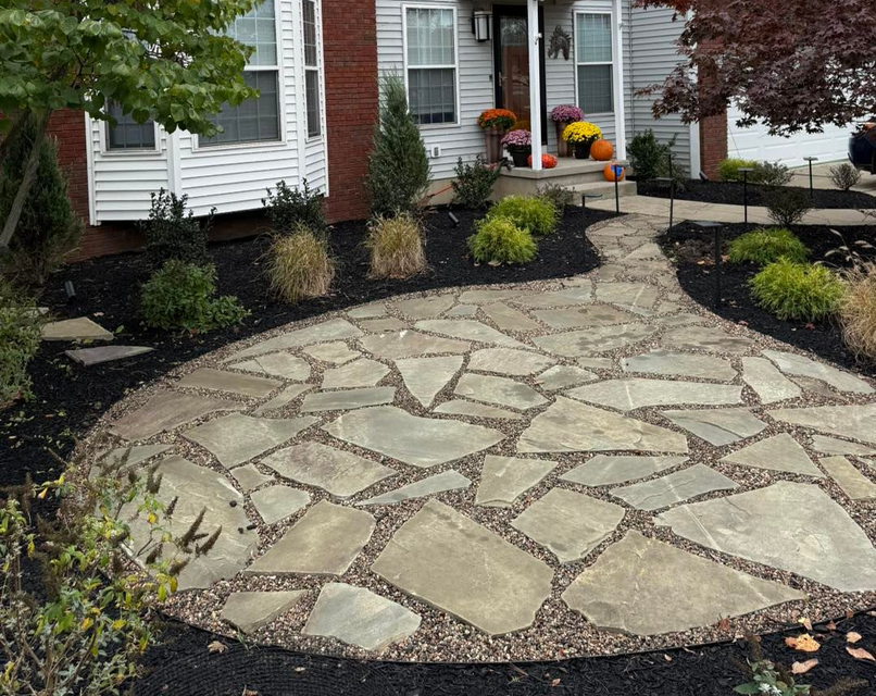 Stone path leading to a two-story house with brick and gray siding. Autumn decorations on porch.